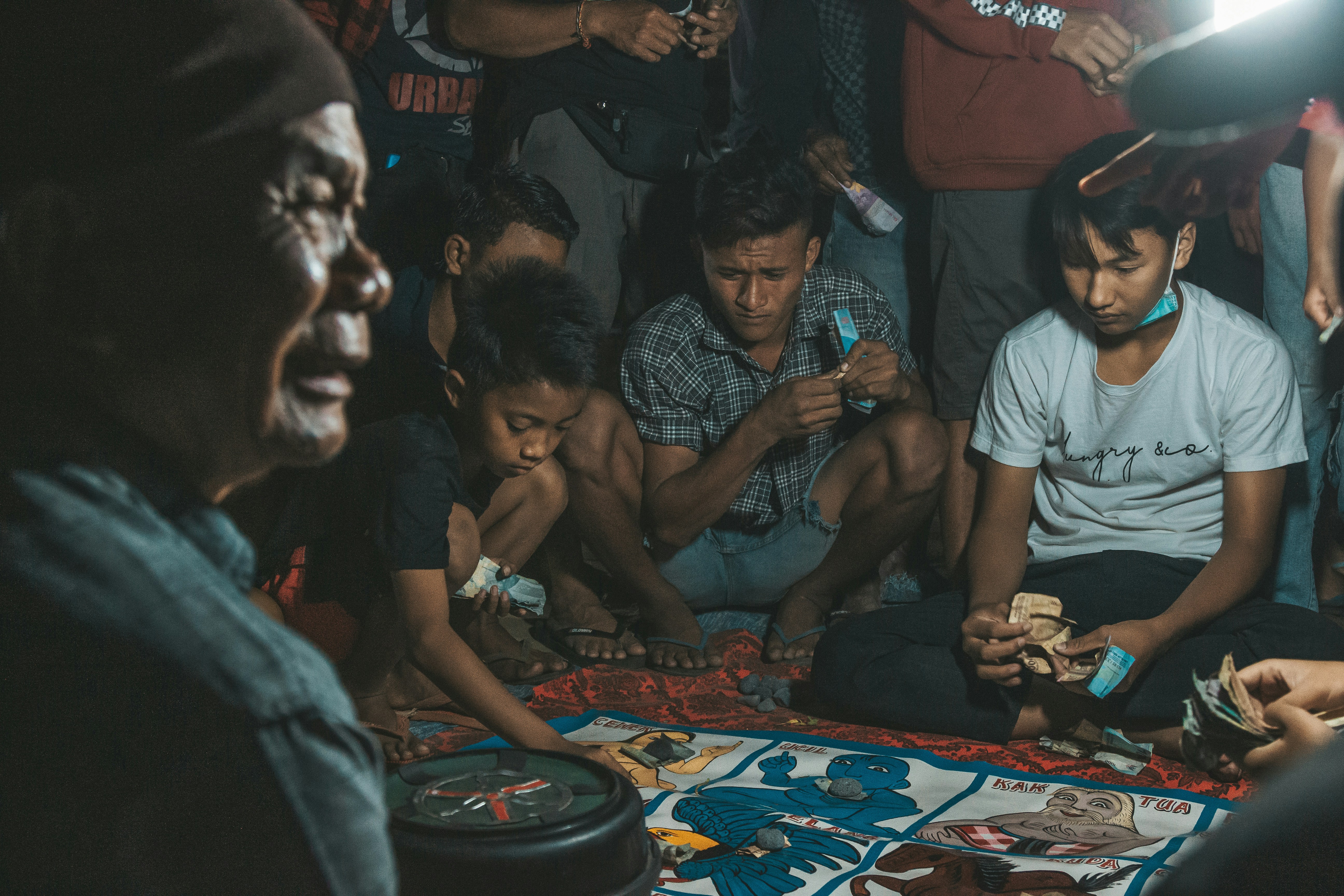 A group of young people in an urban Southeast Asian setting engrossed in mobile gaming on their smartphones.